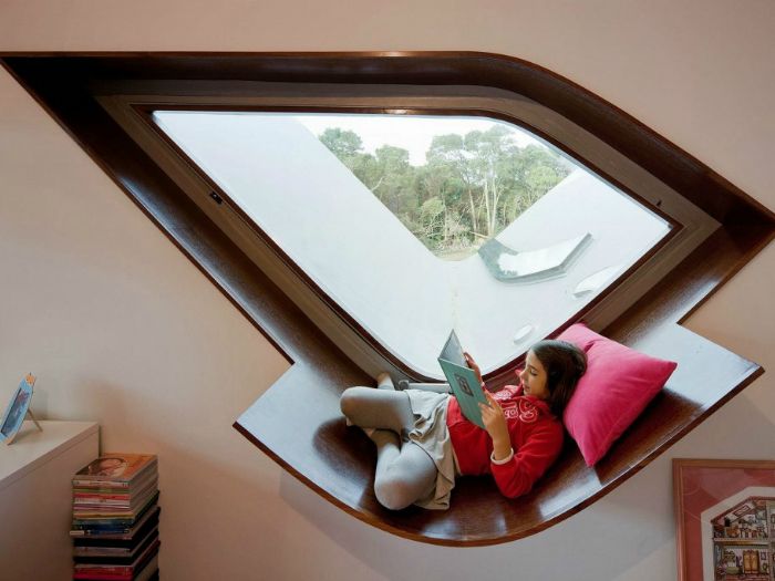 Een raam met een originele vorm en een vensterbank uitgerust om te lezen en te ontspannen.